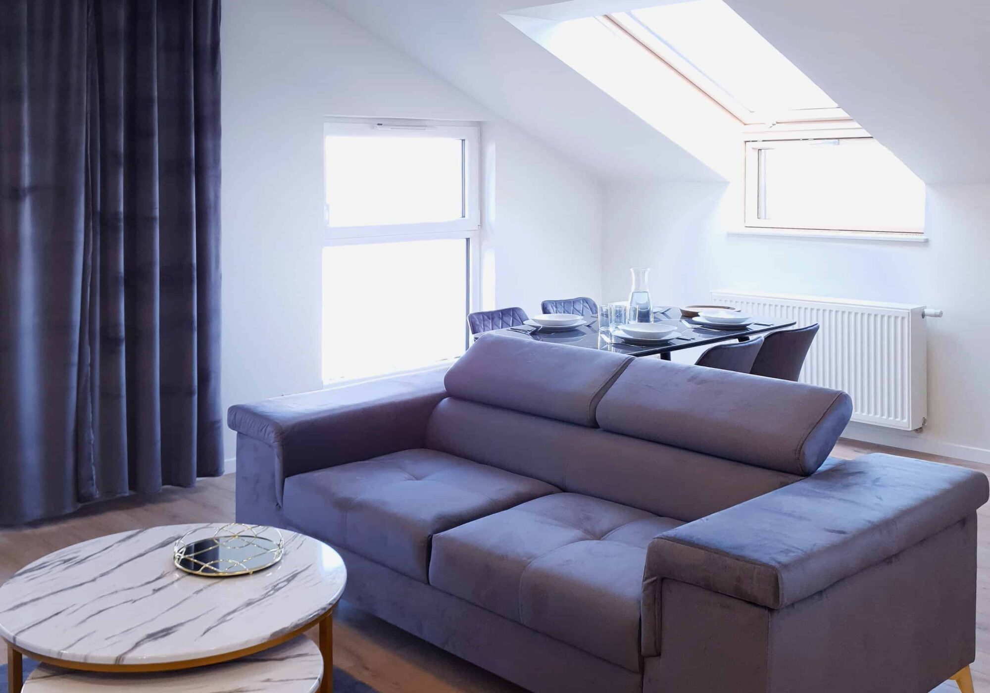 Szara sofa w salonie, szary dywan, jasne panele podłogowe.